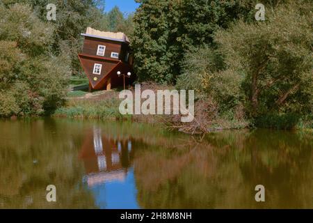 Malerischer Blick auf die Fee. Ein auf den Kopf gedrehtes Haus, ein umgestürzter Baum und ihre Spiegelungen in der Wasseroberfläche des Flusses. Stockfoto