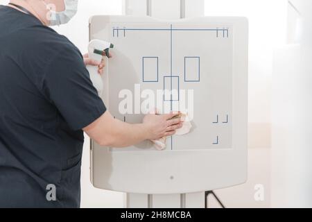 Der Arzt reinigt das Röntgengerät. Röntgenabteilung im modernen Krankenhaus. Röntgenraum mit Scangerät und leerem Bett. Techniker, der eine Röntgenaufnahme anpasst Stockfoto