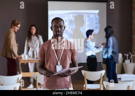 Porträt eines jungen afrikanischen Geschäftsmannes, der seinen Bericht in der Kamera hält und an einem Geschäftsseminar teilnimmt Stockfoto