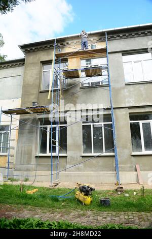 Fassadengestaltung und Renovierung. Ein Bauunternehmer auf Gerüsten ist mit Stuck fertig, putzt die Außenwand des Hauses vor dem Lackieren. Stockfoto