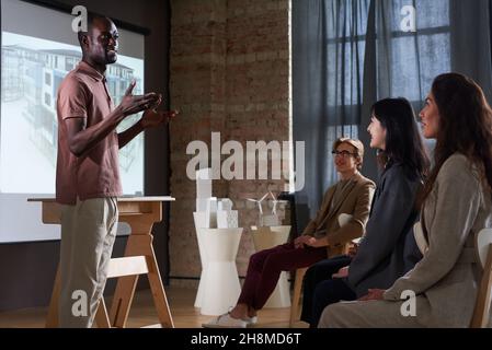 Afrikanischer junger Architekt, der den Kollegen auf der Konferenz ein Architekturprojekt vorstellt Stockfoto
