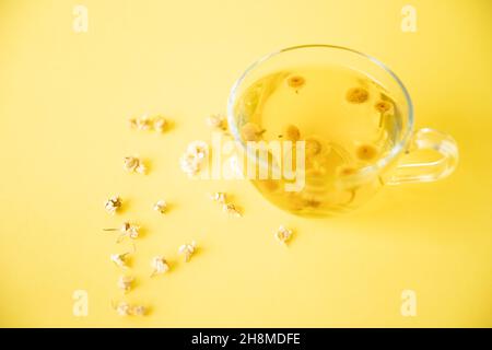 Kamillentee, der auf gelbem Hintergrund gebraut und in einer Glasschale serviert wird Stockfoto