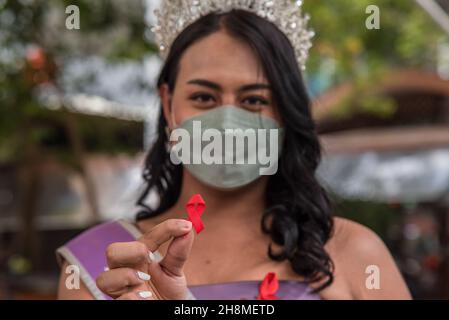 Panurat Noibunjong 'Miss LGBT Thailand Friendship 2021' hält ein rotes Band mit einem gekrümmten Kreuz, das symbolisch für den Welt-Aids-Tag während der Kampagnen zum Welt-Aids-Tag 2021 steht.die Kampagnen zum Welt-Aids-Tag 2021 wurden im Distrikt Ratchathewi, Bangkok, am Siegesdenkmal anlässlich des Welt-AIDS-Tages 2021 abgehalten. Das Thema des Welt-Aids-Tages 2021 der Weltgesundheitsorganisation (WHO) lautet „Beseitigung von Ungleichheiten. End AIDS“. „mit einem besonderen Fokus darauf, die zurückgelassenen Menschen zu erreichen und die wachsenden Ungleichheiten beim Zugang zu wichtigen HIV-Dienstleistungen hervorzuheben. Stockfoto