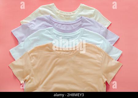 Mehrfarbige T-Shirts Pastellfarben Beige Weiß Lila.T-Shirts Mockup für Design auf Farbe Koralle rosa Hintergrund. Gestapelte Basic T-Shirts Stockfoto