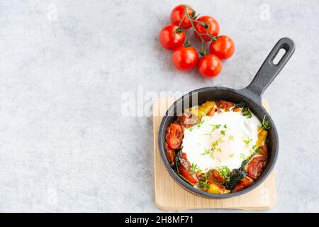 Gebackenes Ei mit Gemüse in einer Pfanne mit Gartenkresse bestreut. Shakshuka mit Tomaten, Paprika, Spinat und Microgreens auf grauem Hintergrund. Stockfoto