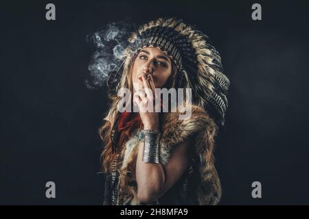 Schöne schamanische Mädchen im Studio auf schwarzem Hintergrund mit Zigarette in der Hand. Stockfoto