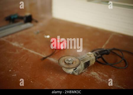 Schleifwerkzeug mit Schleifscheibe und anderen Werkzeugen auf dem schmutzigen braunen Boden. Stockfoto