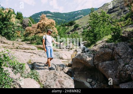 Männlicher Besitzer eines Spanielhundes, der gegen Berge und Wasserfall läuft. Stockfoto