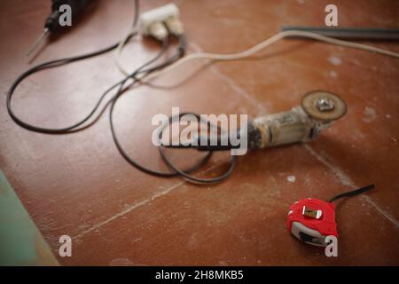 Rotes Messgerät, Schleifwerkzeug mit Schleifscheibe und anderen Werkzeugen auf dem braunen Holzboden. Stockfoto