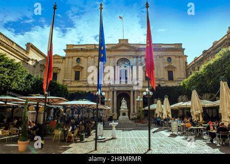 Blick auf das Gebäude der Nationalbibliothek von Malta, davor Marmorskulptur der Königin Victoria, im Vordergrund Fahnenmast, auf der Seite Touristen hinein Stockfoto