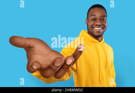 Glücklicher schwarzer Kerl, der große ausgestreckte Hand zeigt, Hilfe anbietet, etwas nimmt oder gibt und nach Unterstützung greift Stockfoto