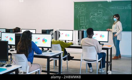 Multirassische Studenten, die während der Business Class Computer mit Sicherheitsmasken in der Schule benutzen - Fokus auf afrikanischen Mann zurück Stockfoto