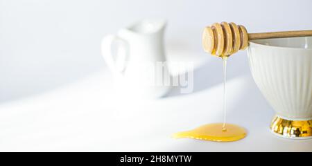 Honig fließt aus gedrehtem Honigstock. Honigs tun auf weißem Hintergrund. Frühstücksahnekännchen Stockfoto