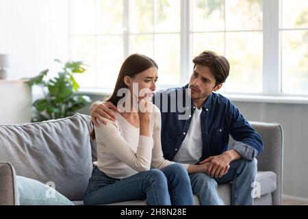 Serious vorsichtig jungen europäischen Kerl beruhigt verärgert unglückliche Dame im Wohnzimmer Interieur Stockfoto
