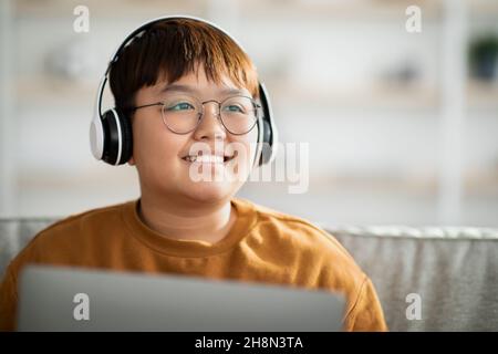 Nahaufnahme eines fröhlichen asiatischen Kindes mit schnurlosem Headset mit Laptop Stockfoto