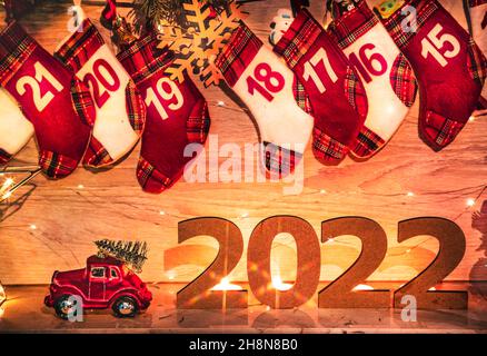 Weihnachtskarte mit Girlande-Lichtern für das neue Jahr 2022. Adventskalendersocken und eine Schachtel mit Geschenken am Kamin. Weihnachten und Silvester. De Stockfoto