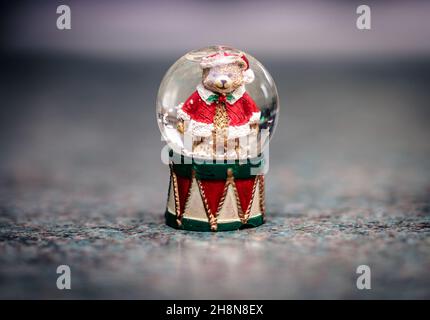 Winterlicher Weihnachts-Teddybär in einem Weihnachtsmann-Outfit in einer Schneekugel. Stockfoto