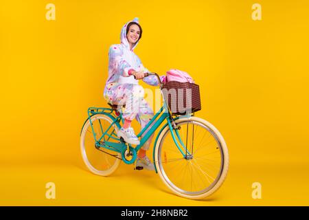 In voller Länge Körpergröße Foto Frau im Einhorn Kostüm lächelnd Reiten Fahrrad isoliert leuchtend gelbe Farbe Hintergrund Stockfoto