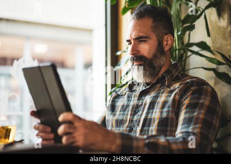 Der Erwachsene Mann sitzt im Café und benutzt ein digitales Tablet. Stockfoto