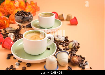 Kaffee, Schokolade, Kaffeebohnen und Blumen. Espresso mit Schaum oder Macchiato in kleinen Tassen, bestreute Kaffeebohnen und Pralinen. Hochwertige Fotos. Speicherplatz kopieren Stockfoto