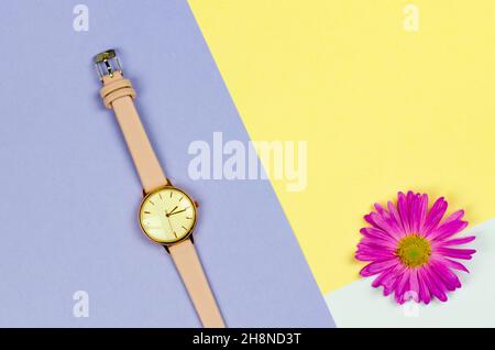 Stilvolle Damen Uhr auf einem farbigen Hintergrund mit Blumen und Platz für Text. Uhr mit einem rosa Armband Stockfoto