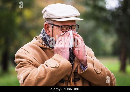 Außenportrait eines älteren Mannes, der im Winter im Park die Nase bläst. Stockfoto