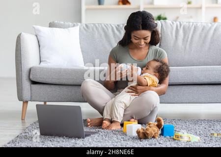 Mutterschaftsurlaub Konzept. Junge Schwarze Mutter Gibt Dem Baby Flasche Mit Wasser Stockfoto