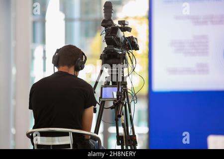 Camcorder Operator filmt Live-Show auf einem Stuhl sitzend. Stockfoto