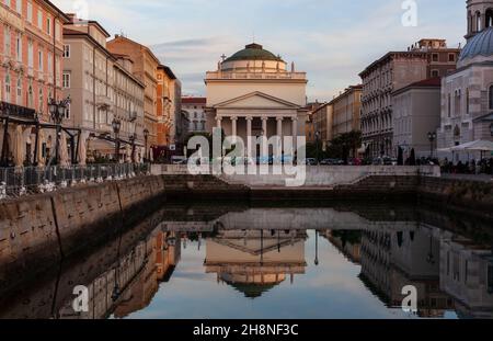 Panoramablick auf den Gran Canale in Triest bei Sonnenuntergang. Die Kirche St. Antonio Thaumaturgo spiegelte sich auf dem Wasser des Canale Grande Stockfoto