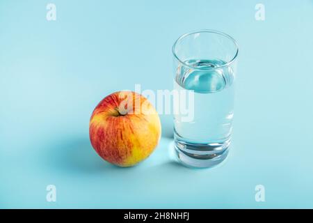 Apfel und Glas reines Wasser auf blauem Hintergrund. Gesundheit und Ernährung Konzept, Ort für Text. Stockfoto