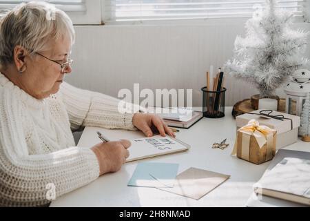 Gesunde Neujahrvorsätze für ältere Erwachsene. Ältere ältere alte Frau in weißem Pullover schreiben handschriftlichen Text My Goals in offenen Notizblock auf dem Stockfoto