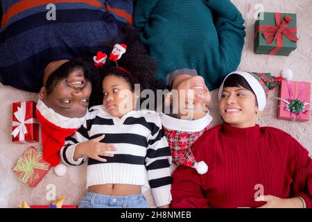 Glückliche afrikanische Familie liegt lächelnd am Weihnachtstag zusammen, während Geschenkbox auf dem Boden, Draufsicht, Beziehung und Bindung der Familie, Feier und ho Stockfoto