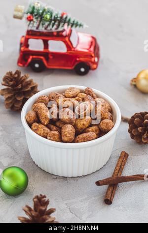 Kandierte oder gezuckerte Mandeln mit Honig und Zimt in kleiner Porzellanschale auf grau mit weihnachtlicher Dekoration. Traditionelle Weihnachtsbonbons für den Urlaub. Speicherplatz kopieren Stockfoto