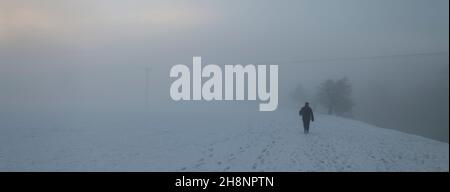 Einzelfigur eines Mannes, der in starkem Nebel am Flussufer entlang läuft, Ribble Valley, Lancashire, Großbritannien. Stockfoto