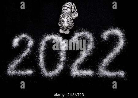 Frohes Neues Jahr 2022. Chinesisches Neujahr 2022. Toy Tiger und das Datum 2022 ist mit Salz wie Schnee geschrieben, isoliert auf schwarzem Hintergrund, Draufsicht. Stockfoto