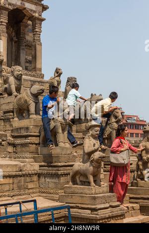 Eine Frau mit ihren Kindern auf den Stufen des Hindu-Tempels Siddhi Laxmi auf dem Durbar-Platz. Bhaktapur, Nepal. Ihre Jungen klettern auf die Statuen. Stockfoto