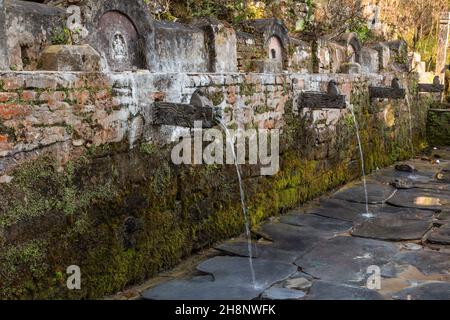 Geschnitzte Steindrachen sprudeln Quellwasser am Teendhara-Brunnen im Newari-Dorf Bandipur, Nepal. Stockfoto