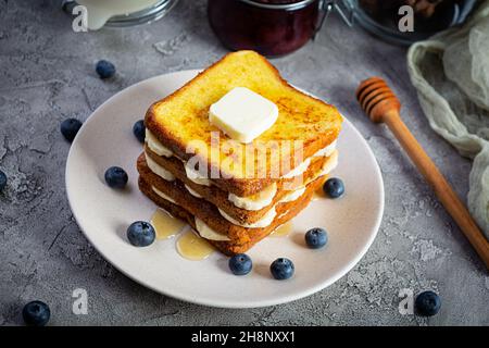 French Toast mit Banane, Heidelbeere, Honig und Erdbeermarmelade. Köstliches Frühstück oder Brunch mit Toast und Keksen Stockfoto