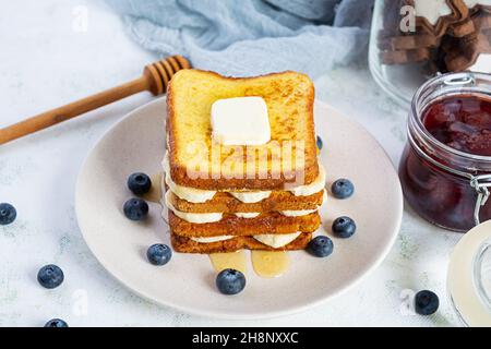 French Toast mit Banane, Heidelbeere, Honig und Erdbeermarmelade. Köstliches Frühstück oder Brunch mit Toast und Keksen Stockfoto