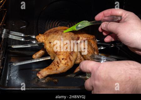 Männliche Hände decken rohes ganzes Huhn, das im Ofen mit Sauce röstet, aus nächster Nähe. Ein Fleischgericht für ein festliches Abendessen vorbereiten. Natürliche hausgemachte gesund Stockfoto