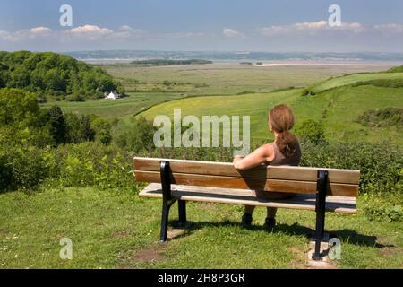 Frau, die auf einer Bank in Llanmadoc sitzt und einen weitreichenden Blick auf Llanridian Sands, Burry Port, Gower Peninsula, Südwales, Großbritannien bietet Stockfoto