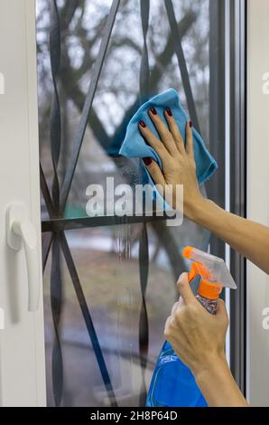 Frau mit einem Lappen wäscht das Glas mit einem Glasreiniger. Hochwertige Fotos Stockfoto