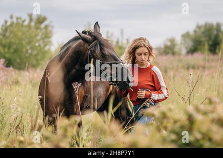 Junge Frau geht mit Pferd über Feld, Wiese, Lifestyle mit Kopierraum. Stockfoto