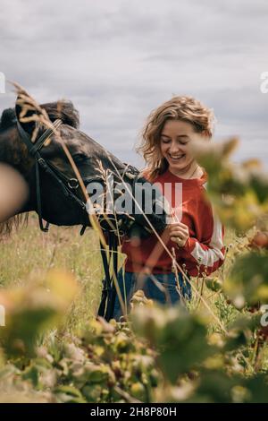 Frau lacht auf Pferd im Feld, Lifestyle, Vertikalaufnahme. Stockfoto