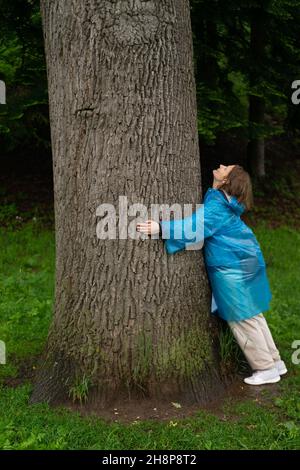 Junge Frau, die sich im Sommerwald an den Baumstamm lehnt. Stockfoto