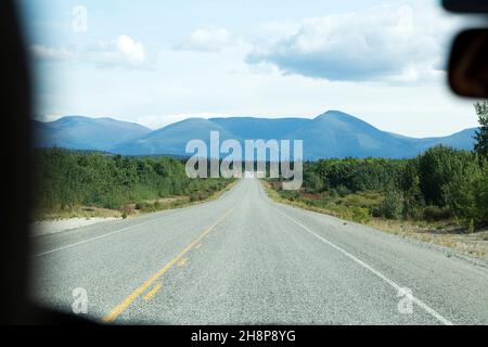 Der Alaska Highway durch die Windschutzscheibe eines Fahrzeugs, das im Yukon, Kanada, fährt. Das Fahrzeug befindet sich auf einer Autoreise. Stockfoto