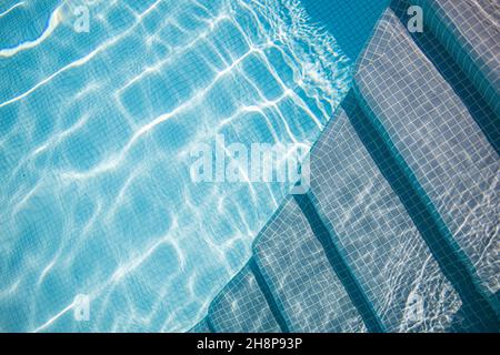 Rand des blauen Swimmingpools. Sommer Wassersport, Freizeit Hintergrund. Textur der Wasseroberfläche, blau türkis lebhaft hell sonnig in der Nähe Treppe Stockfoto