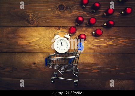 Wecker mit Mitternachtsanzeige, kleinem Wagen und bunten Weihnachtskugeln auf einem Holzhintergrund. Dunkler Weihnachtshintergrund. Stockfoto