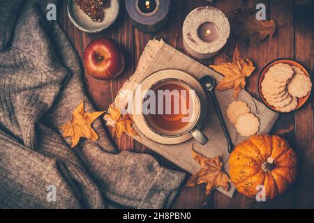 Heißer Tee mit Keksen, Apfel- und Herbstlaub und Kürbissen auf Holzgrund Stockfoto