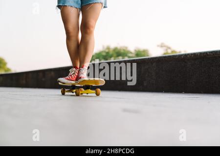 Zugeschnittenes Bild einer jungen Frau, die auf einem Skateboard im grünen Park reitet Stockfoto